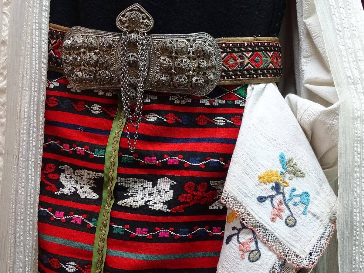 Detail pakaian tradisional dengan sabuk logam berukir dan kain bordir warna-warni khas kerajinan tangan Veliko Tarnovo.