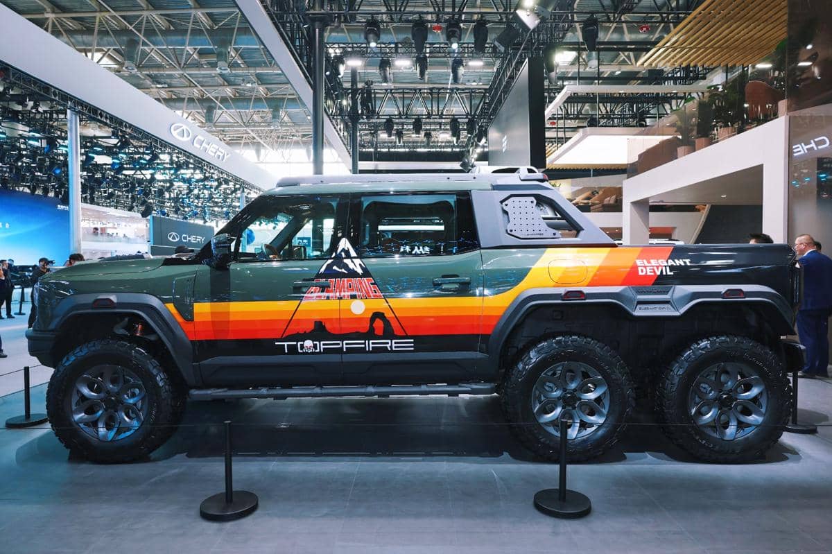 Mobil off-road beroda enam dengan desain gagah dan grafis warna-warni dipamerkan di sebuah ajang otomotif dalam ruangan.