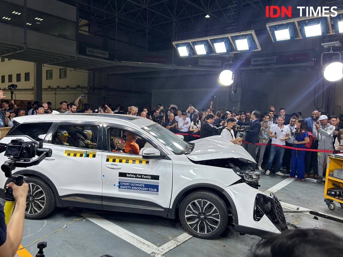 Mobil Chery Tiggo 9 berwarna putih mengalami uji tabrak di dalam ruangan dengan banyak penonton dan fotografer yang mengamati hasilnya.
