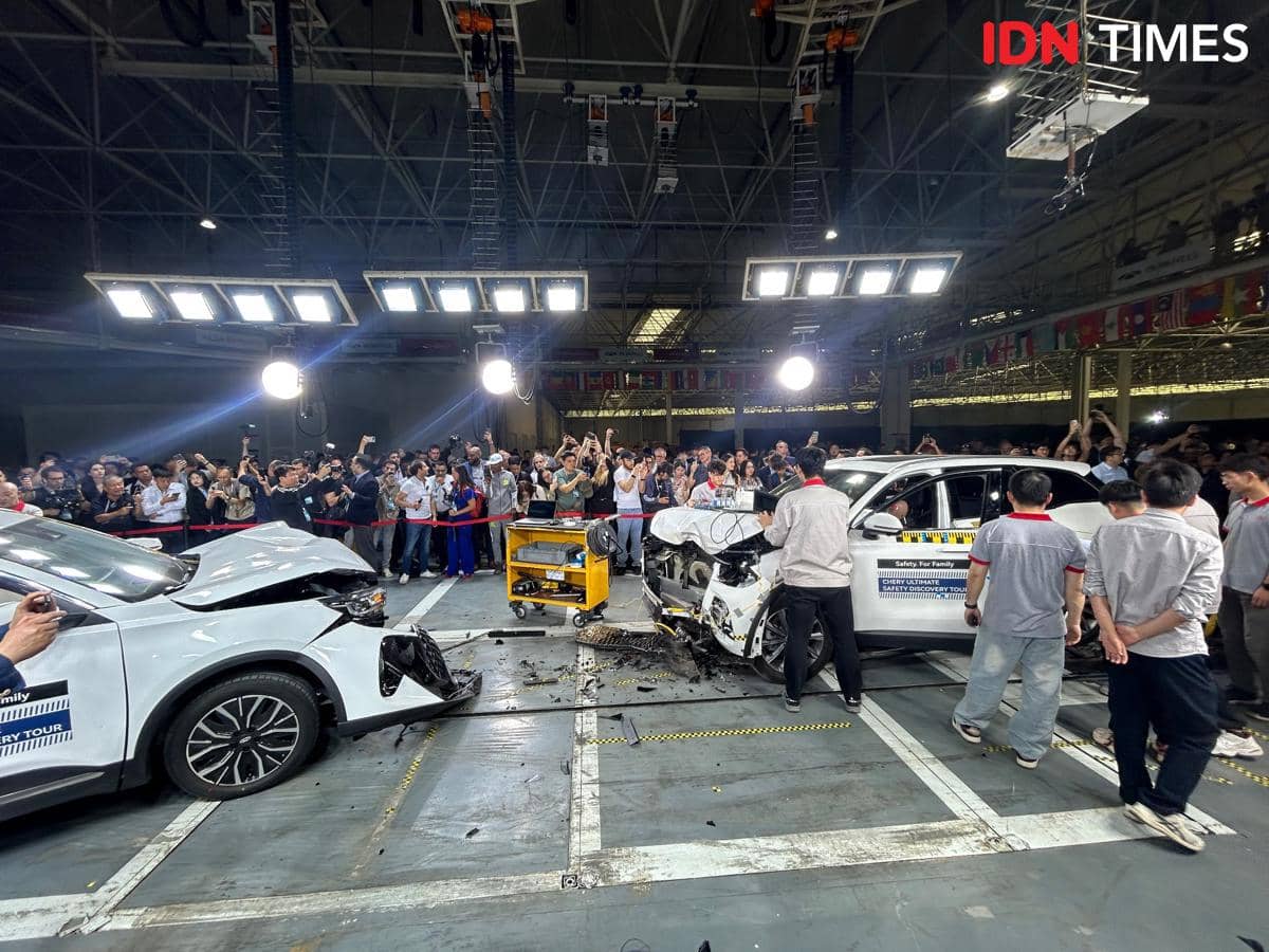 Dua mobil putih bertabrakan dalam uji tabrak di dalam gedung besar di Wuhu, China, disaksikan banyak orang dan teknisi.