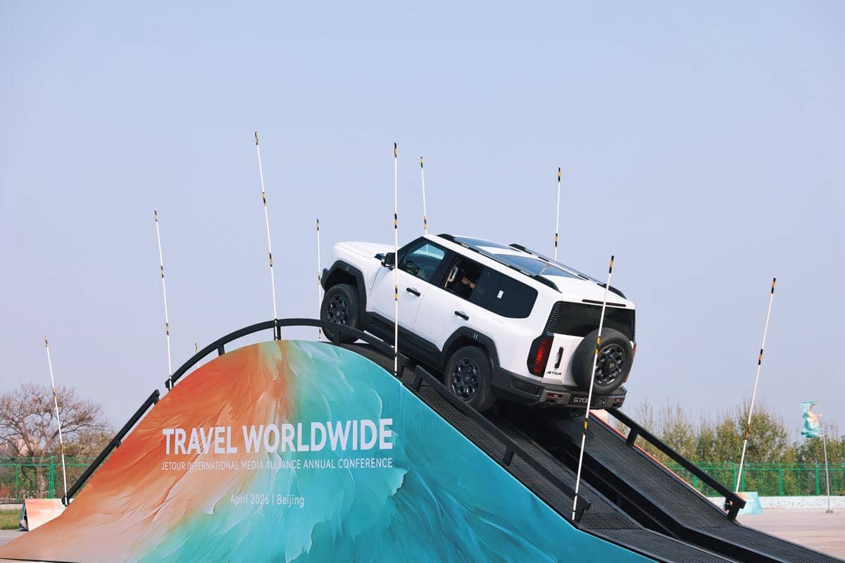 Sebuah SUV putih melintasi tanjakan curam pada sesi uji coba berkendara di lintasan dengan latar langit cerah.