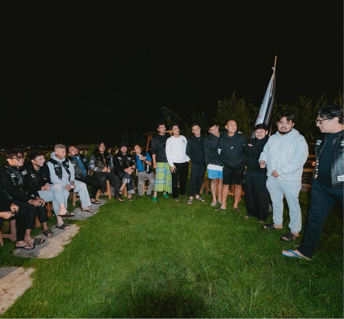 Sekelompok orang mengenakan jaket dan pakaian santai berkumpul di area rumput pada malam hari saat touring ke Semarang, Dieng, dan Yogyakarta.