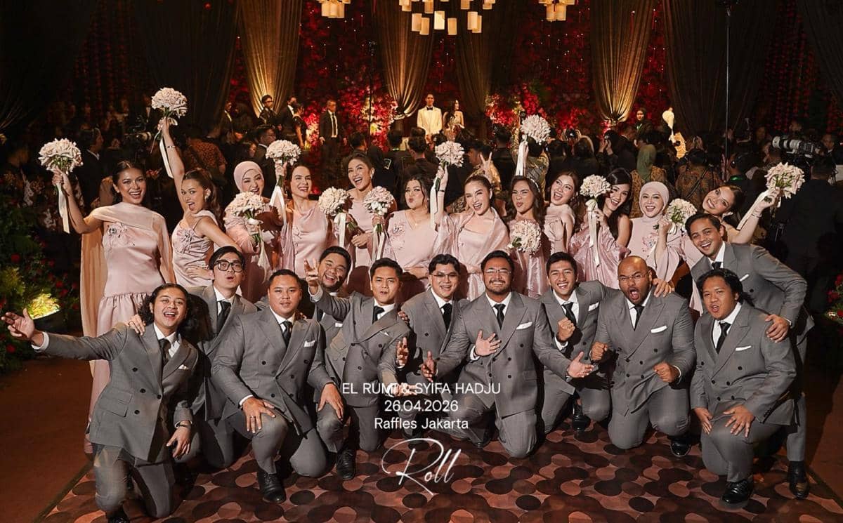 Para bridesmaid mengenakan gaun berwarna pink dan groomsmen mengenakan setelan abu-abu berpose bersama di pesta pernikahan di Raffles Jakarta.