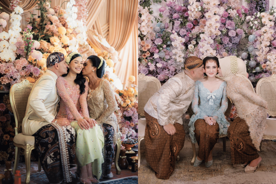 Dua pasangan pengantin mengenakan busana adat Jawa dengan latar bunga berwarna pastel, duduk bersama orang tua dalam suasana bahagia.