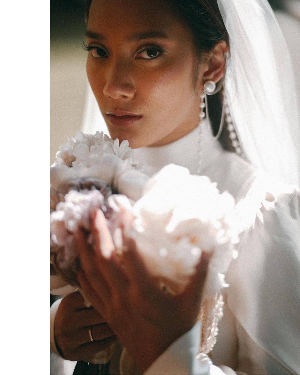 Tara Basro mengenakan gaun putih dan kerudung, memegang buket bunga berwarna lembut dengan ekspresi tenang di wajahnya.