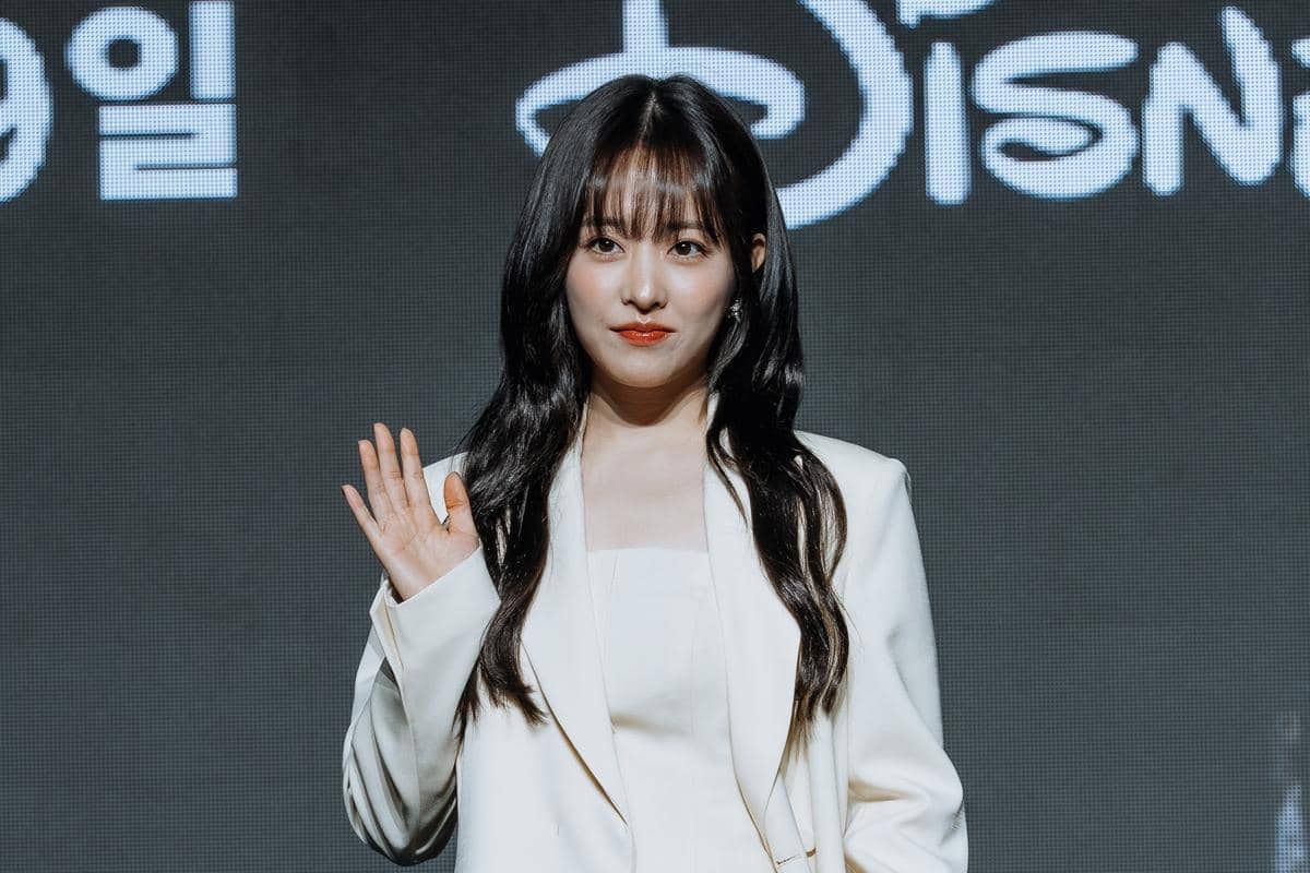 Seorang aktris mengenakan setelan putih berpose sambil melambaikan tangan dalam konferensi pers drama Korea Gold Land.