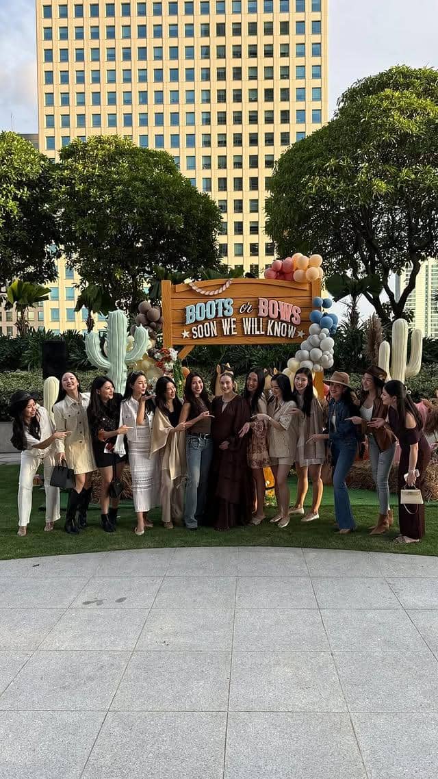 Sekelompok wanita berpose bersama di acara pesta gender reveal bertema western dengan dekorasi balon dan papan kayu bertuliskan 'Boots or Bows'.