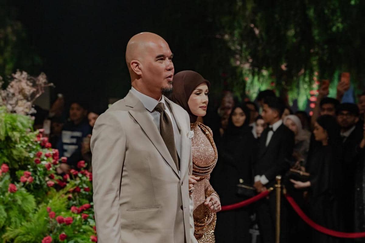 Sepasang tamu berpakaian formal berjalan di karpet merah pada resepsi pernikahan El Rumi dan Syifa Hadju dengan latar tamu undangan.