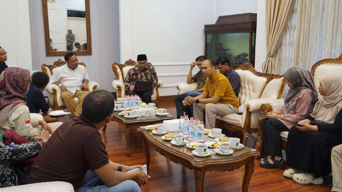 Sejumlah orang duduk berdiskusi di ruang tamu resmi dengan meja berisi minuman dan makanan ringan di Yogyakarta.