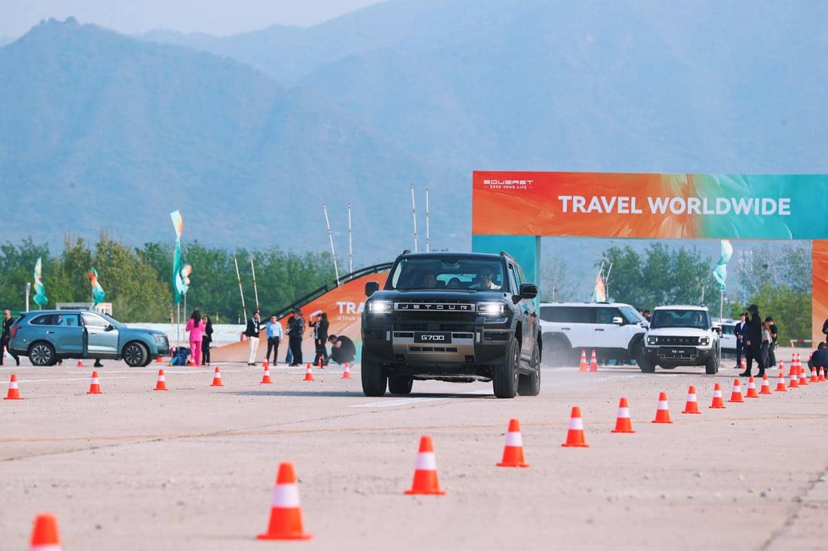 Beberapa mobil SUV Jetour diuji di area terbuka Haidian Airport dengan latar pegunungan dan rambu bertuliskan Travel Worldwide.