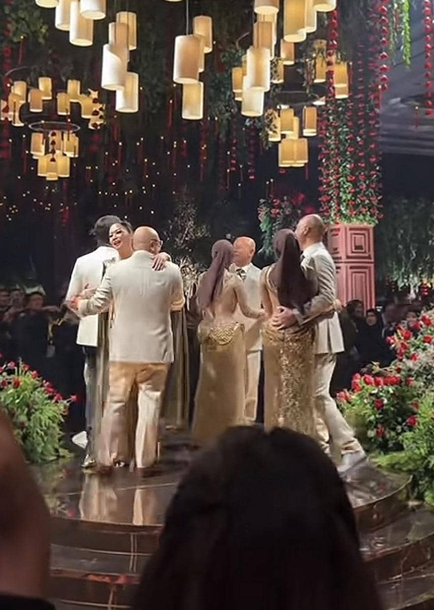 Beberapa pasangan menari di atas panggung berhias lampu gantung dan dekorasi bunga merah serta hijau dalam suasana pesta malam.