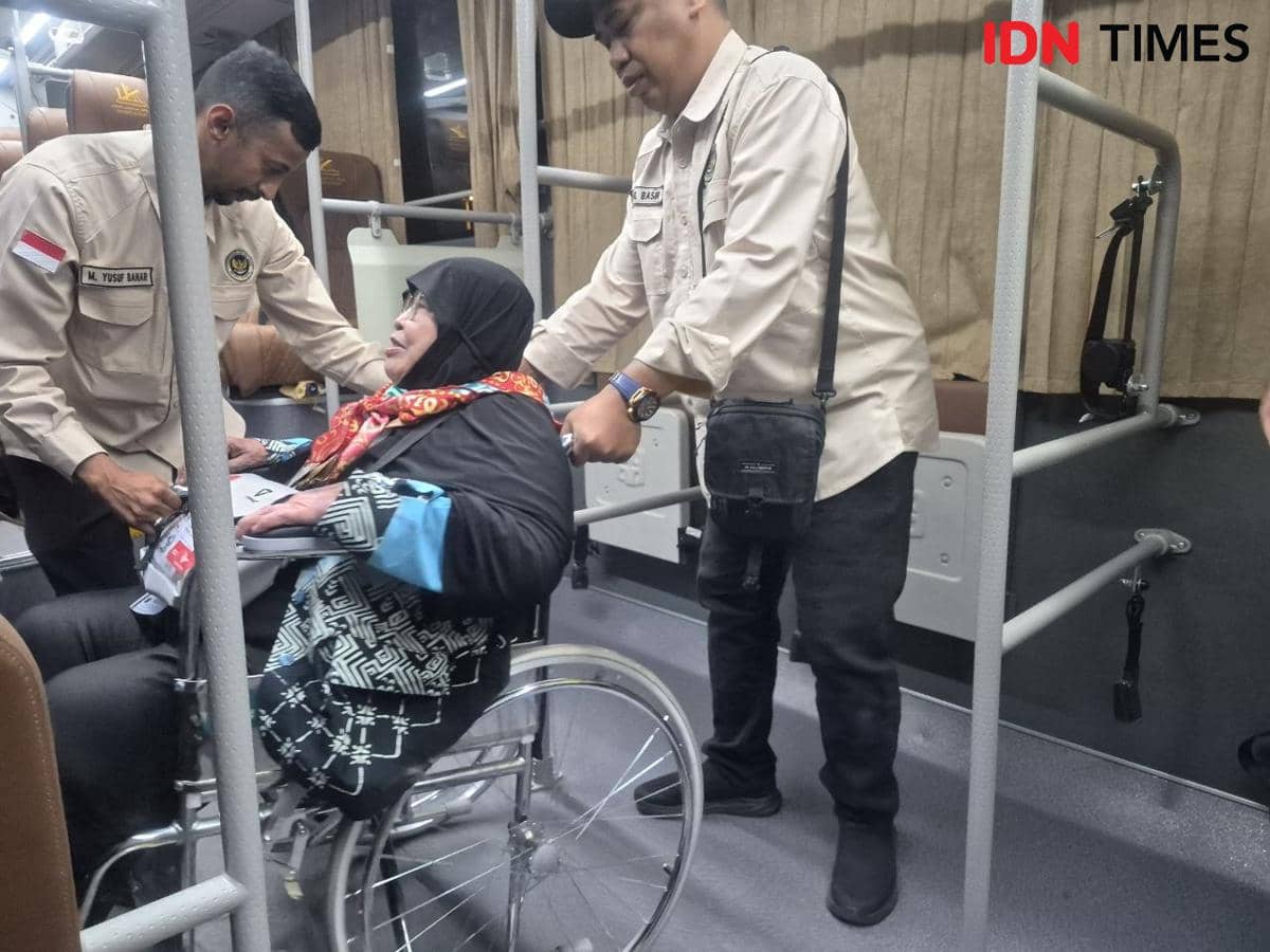 Petugas PPIH Arab Saudi membantu seorang jamaah haji perempuan di kursi roda saat naik ke bus khusus di area bandara.