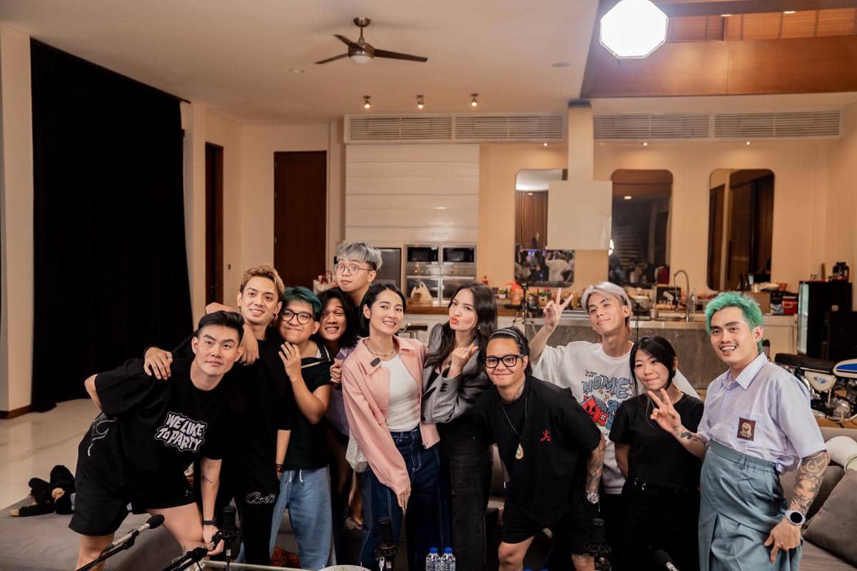 Sekelompok orang berpose bersama di dalam ruangan modern dengan pencahayaan hangat, tampak tersenyum dan bergaya santai di depan kamera.