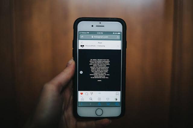 Seseorang memegang ponsel yang menampilkan unggahan puisi di layar Instagram dengan latar belakang kayu berwarna cokelat.