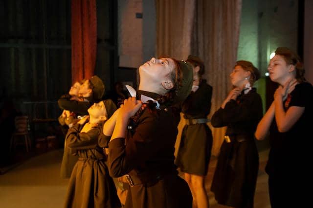 Sekelompok perempuan mengenakan pakaian gelap sedang menampilkan pertunjukan puisi dengan ekspresi dramatis di atas panggung.