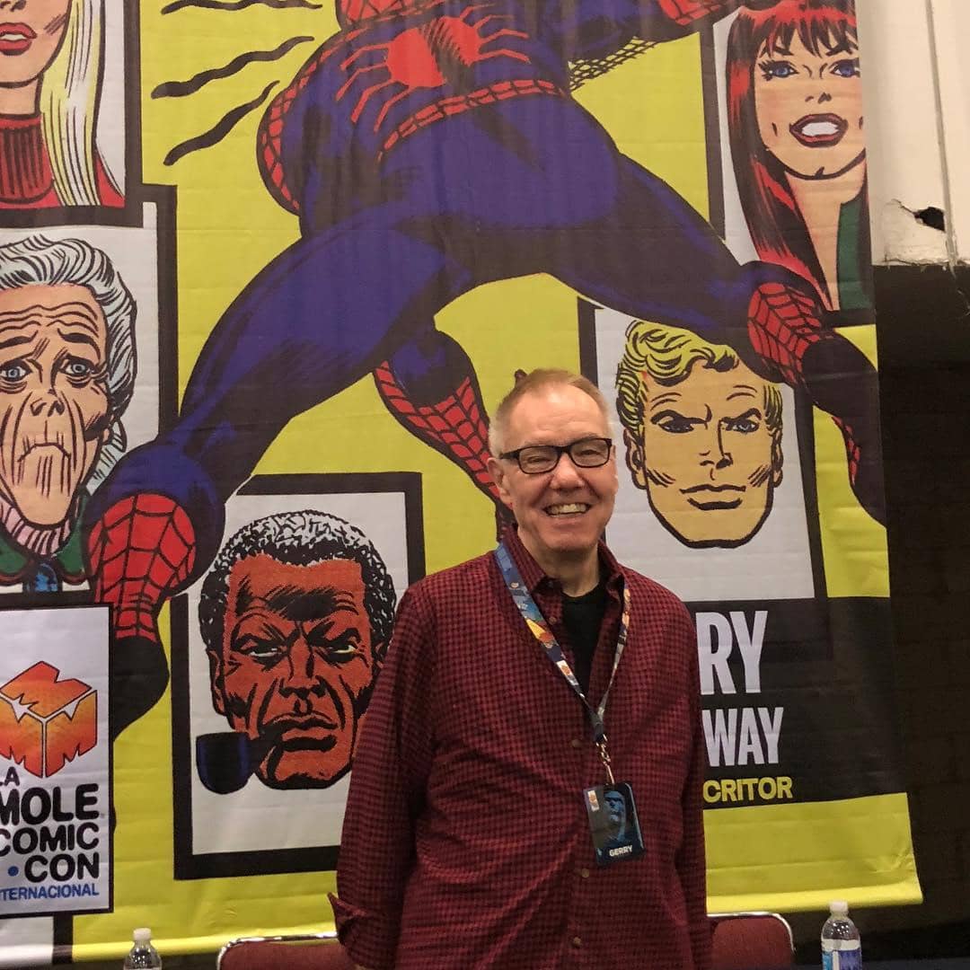 Seorang pria berpose tersenyum di depan spanduk besar bergambar karakter komik Spider-Man dan tokoh lain di acara La Mole Comic Con.