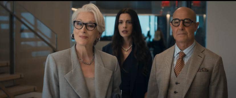 Tiga karakter berdiri di dalam kantor modern dalam cuplikan film The Devil Wears Prada 2, mengenakan busana formal elegan.