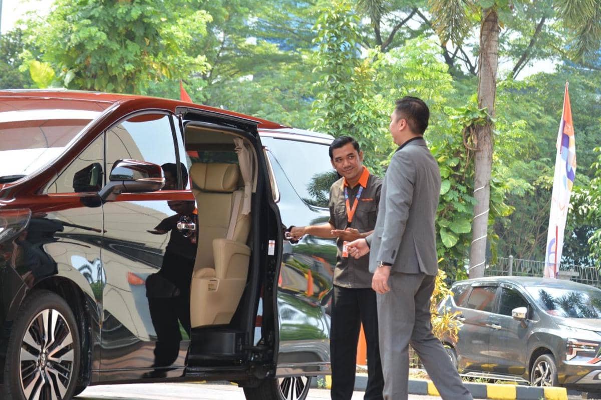 Seorang petugas membuka pintu mobil listrik Maxus Mifa 9 untuk seorang pria di area luar dengan latar pepohonan hijau.