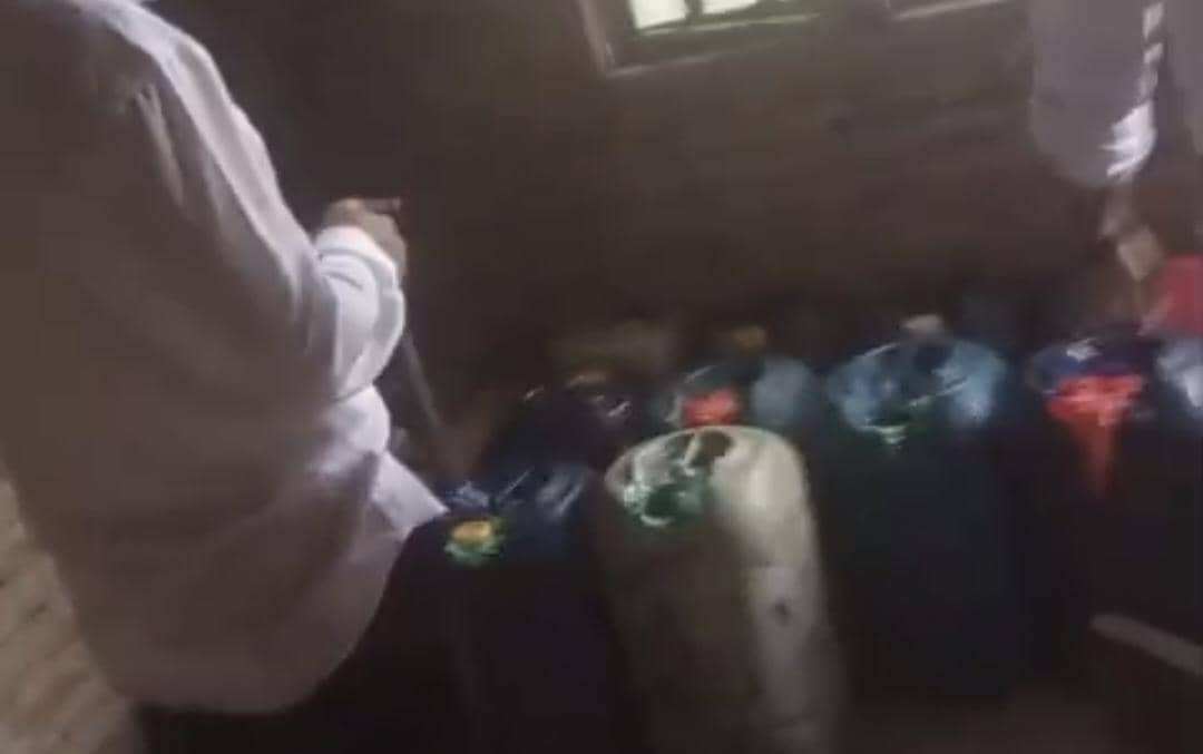 Petugas berdiri di dekat deretan jeriken berisi bahan bakar minyak yang disita di Kabupaten Belu dalam ruangan berpenerangan redup.