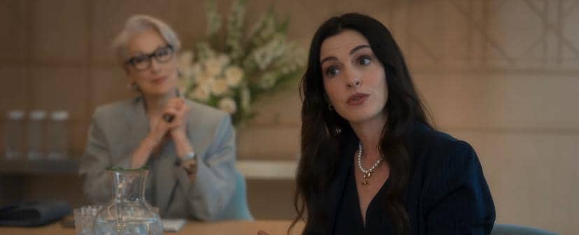 Dua wanita duduk di ruang rapat elegan, salah satunya berbicara dengan ekspresif sementara yang lain memperhatikan dengan tenang.