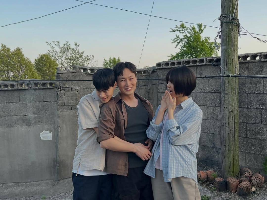 Tiga pemeran drama Korea If Wishes Could Kill tersenyum dan berpose akrab di area luar dengan latar tembok bata abu-abu.