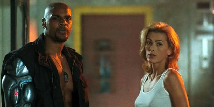 Dua karakter dari film Mortal Kombat Annihilation berdiri di ruangan dengan pencahayaan redup, mengenakan pakaian tempur dan kasual.