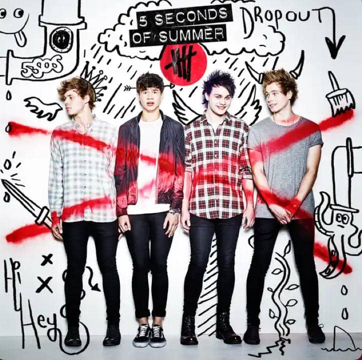 Empat anggota band 5 Seconds of Summer berdiri di depan dinding bergambar doodle hitam putih dengan coretan merah menyilang di latar belakang.