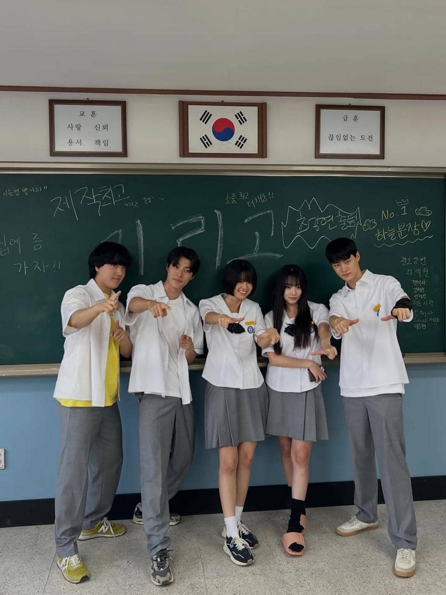 Lima pemeran drama Korea If Wishes Could Kill berpose bersama di depan papan tulis kelas dengan seragam sekolah abu-abu putih.