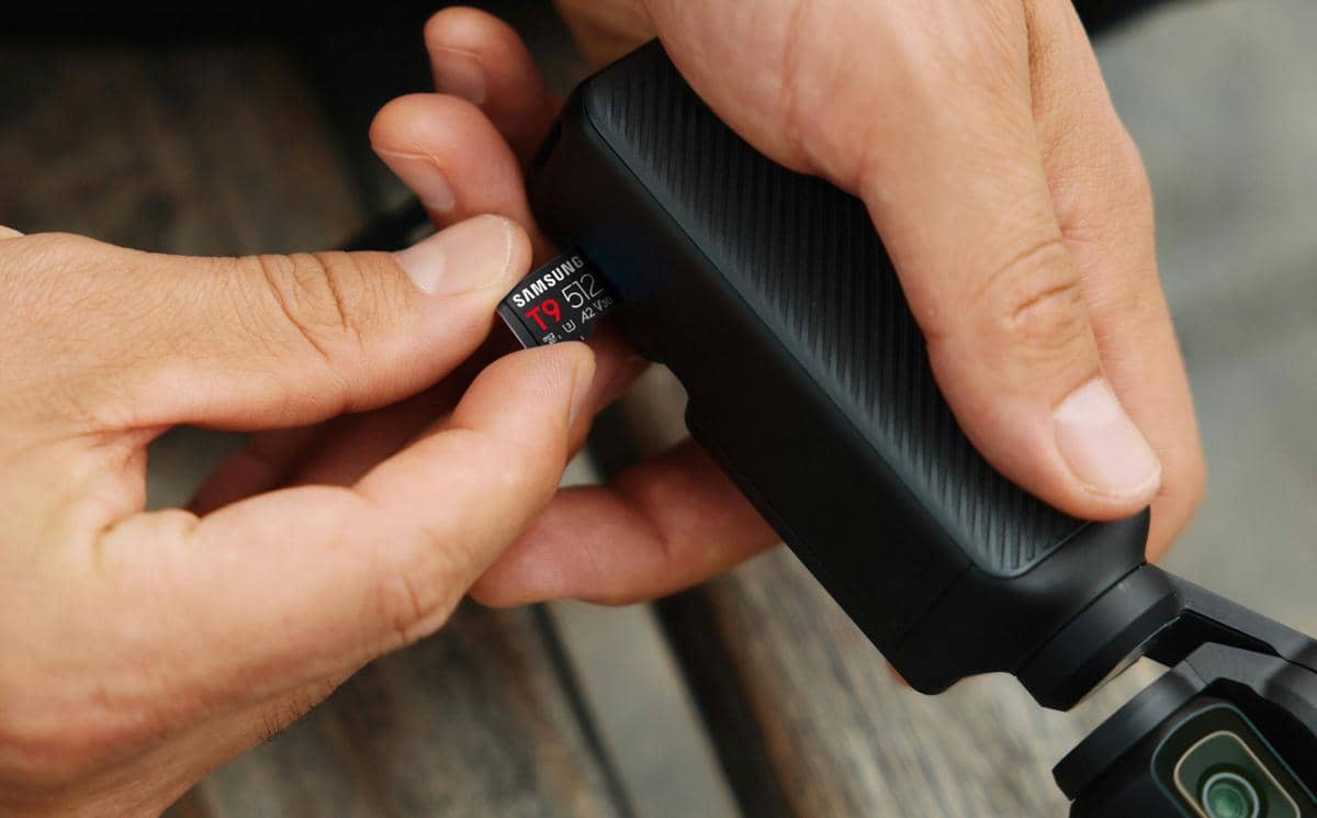 Seseorang memasukkan kartu memori Samsung MicroSD T9 berkapasitas 512 GB ke dalam perangkat kamera hitam portabel.