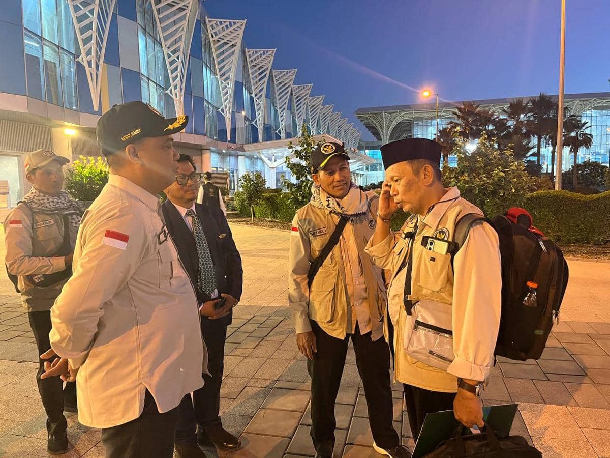 Petugas PPIH menyambut jemaah haji SUB-16 yang baru tiba di Madinah, berbincang di area luar bandara pada malam hari.