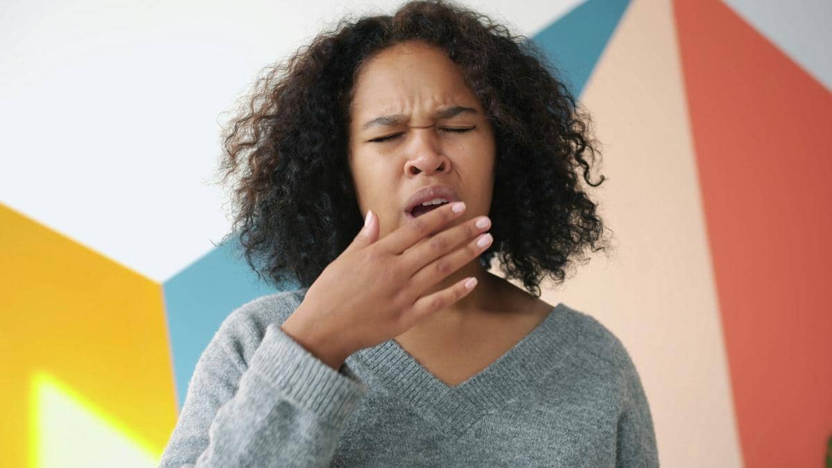 Seorang perempuan mengenakan sweter abu-abu sedang menguap dengan mata tertutup, menggambarkan kondisi lelah akibat kurang tidur.
