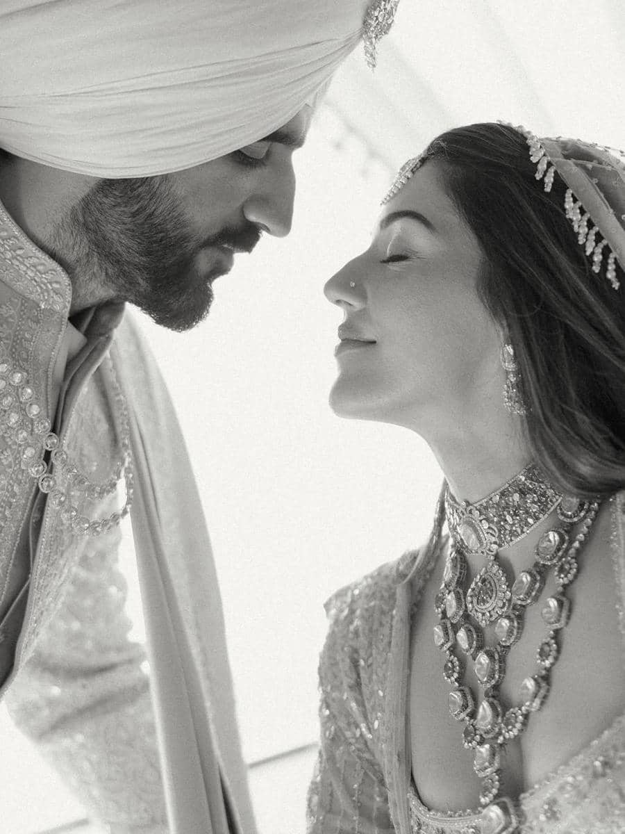 Pasangan pengantin mengenakan busana tradisional India berwarna terang saling menatap dengan lembut dalam suasana pernikahan.