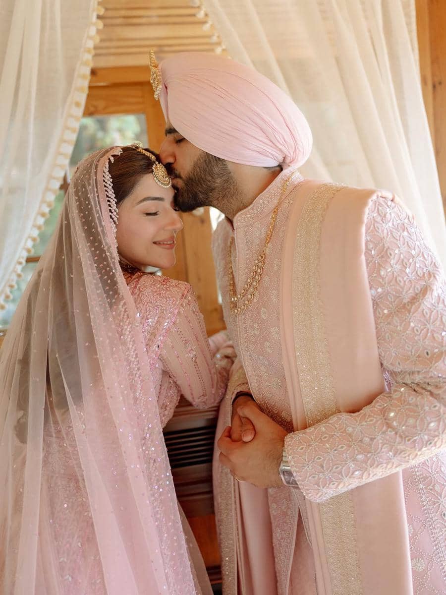 Pasangan pengantin mengenakan busana tradisional India berwarna merah muda lembut, saling berpelukan dengan penuh kasih di hari pernikahan.