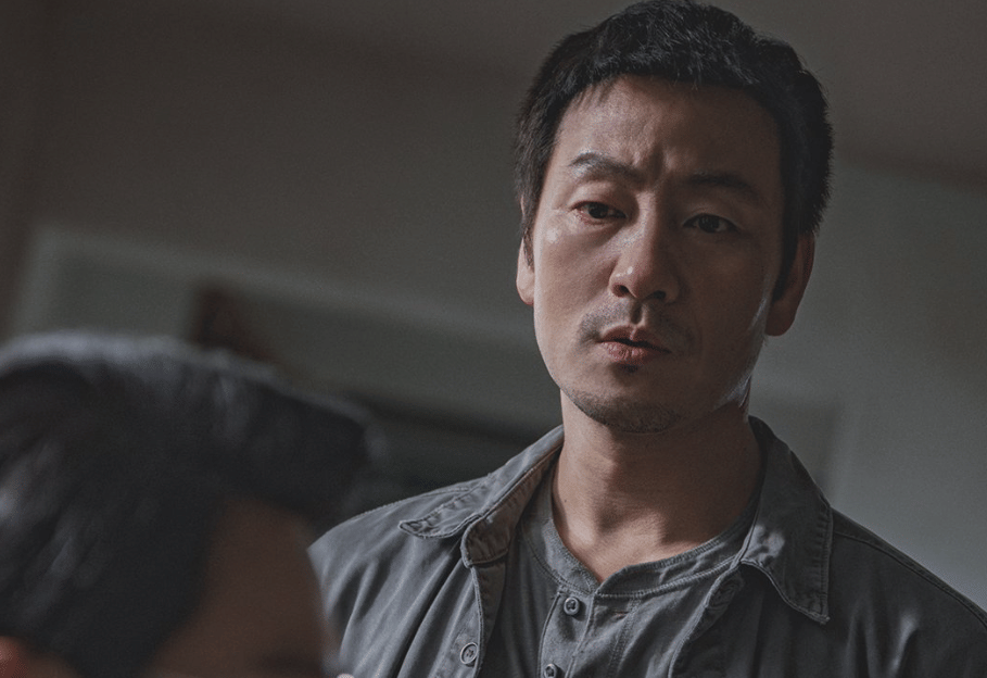 Seorang pria berwajah serius mengenakan kemeja abu-abu dalam cuplikan drama Korea The Scarecrow produksi ENA.