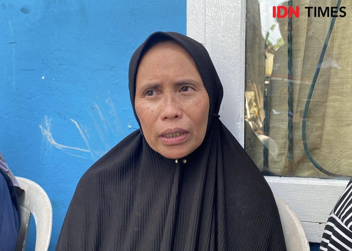 Seorang perempuan berhijab hitam duduk di kursi plastik putih dengan latar dinding biru dan jendela kaca di rumah duka Cipayung, Jakarta Timur.