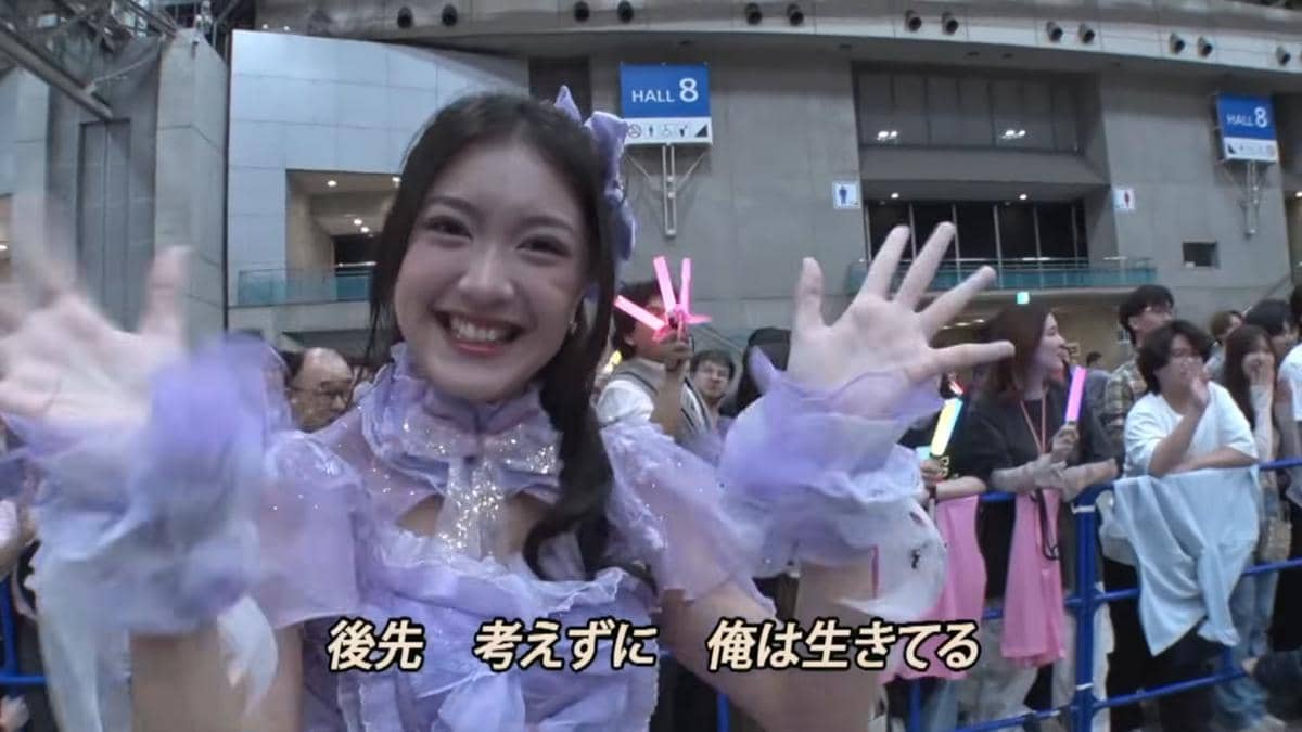 Anggota JKT48 mengenakan kostum ungu tersenyum dan melambaikan tangan kepada penggemar di acara handshake AKB48 2026.