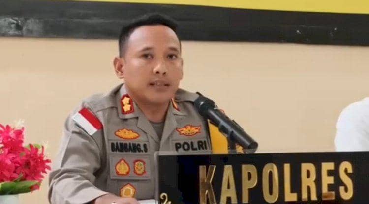 Seorang perwira polisi berseragam duduk di meja dengan mikrofon dan papan nama Kapolres di depannya saat konferensi pers.