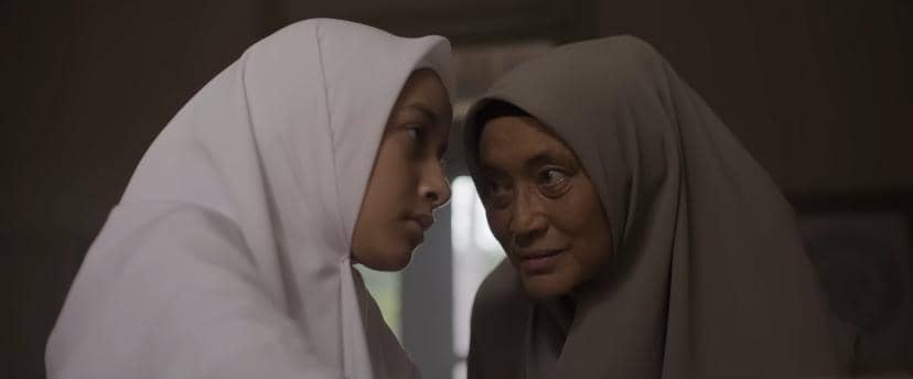 Dua perempuan berhijab saling menatap dengan ekspresi serius dalam adegan film Siksa Kubur produksi Rapi Films.