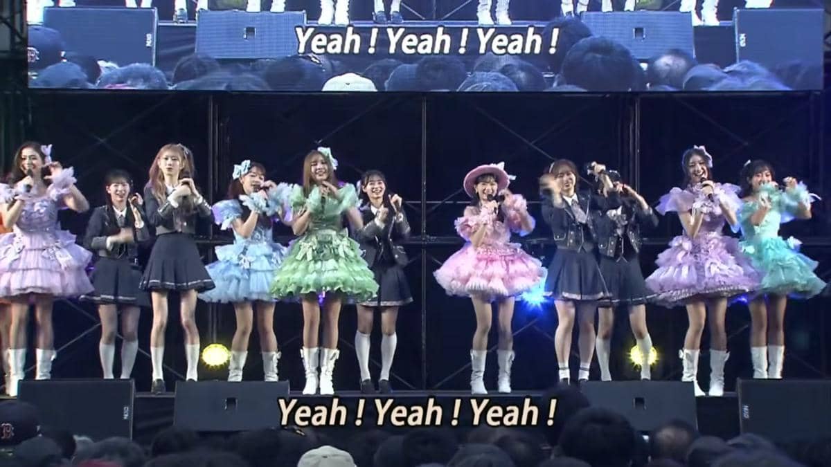 Anggota JKT48 tampil di atas panggung dengan kostum berwarna-warni saat acara handshake AKB48 2026 di depan penonton.