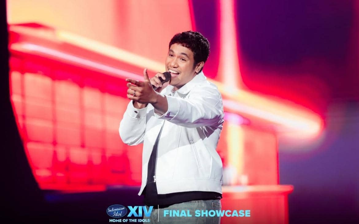 Seorang peserta Indonesian Idol musim ke-14 mengenakan jaket putih sedang bernyanyi di atas panggung dengan latar cahaya merah terang.