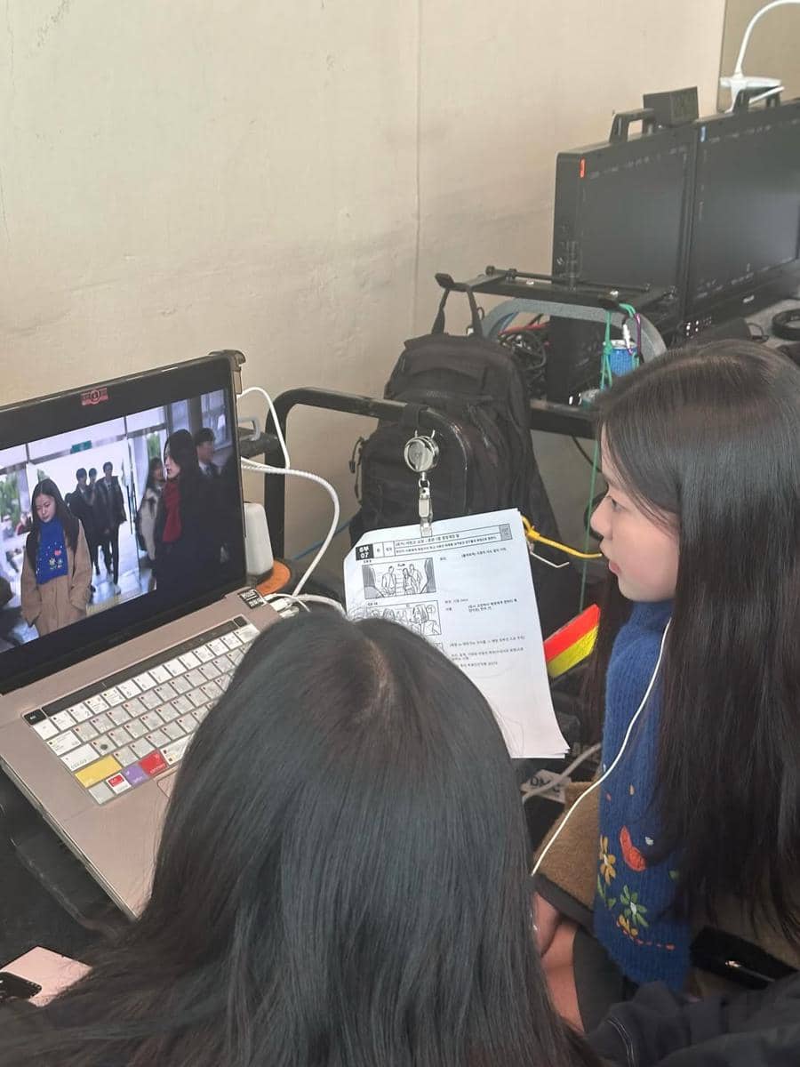 Dua aktris muda memantau adegan di layar monitor sambil memegang naskah di lokasi syuting drama Korea If Wishes Could Kill.