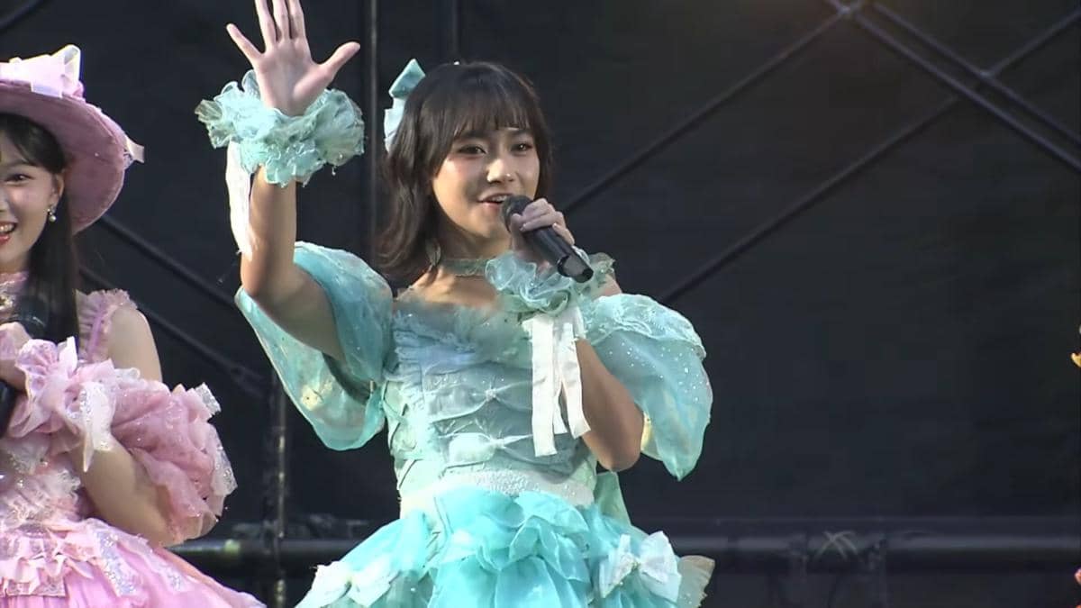 Anggota JKT48 mengenakan kostum biru muda bernyanyi di atas panggung acara handshake AKB48 2026 sambil melambaikan tangan.