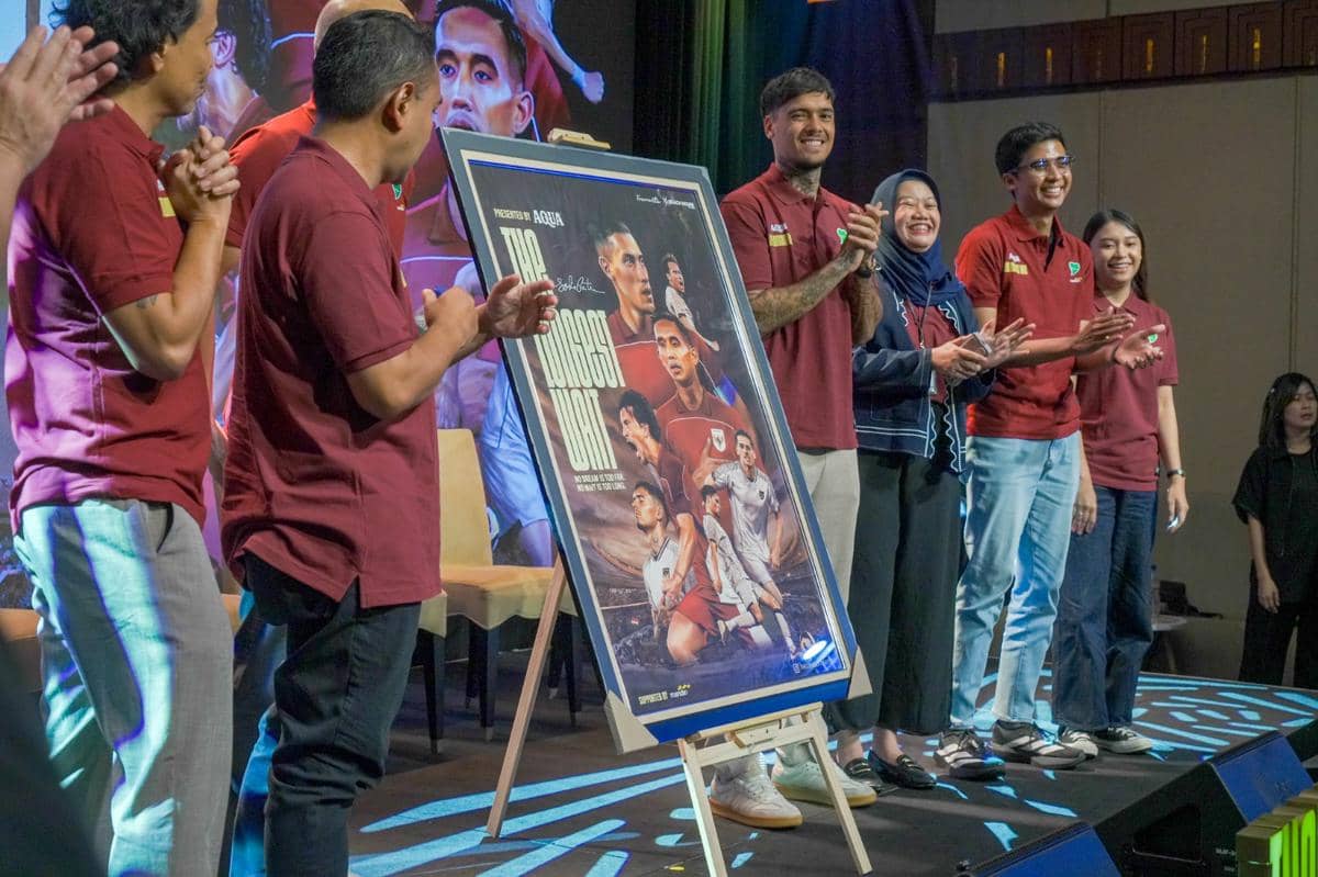 Beberapa orang berdiri di atas panggung mengenakan kaus merah marun sambil memperlihatkan poster film The Longest Wait tentang perjuangan Timnas Indonesia.