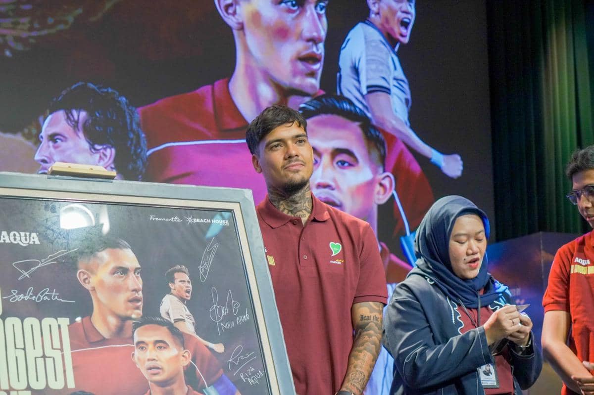 Seorang pria mengenakan kaus polo merah berdiri di depan poster film The Longest Wait bersama dua orang lainnya dalam sebuah acara peluncuran.