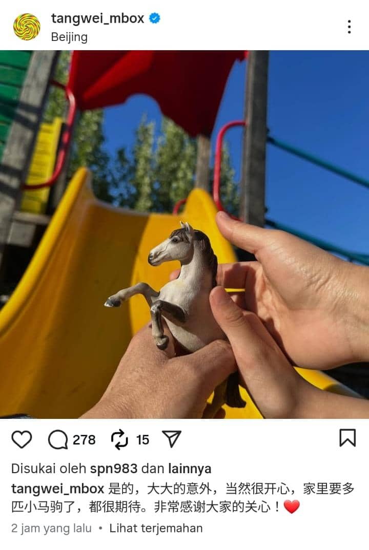 Dua pasang tangan memegang mainan kuda kecil di depan perosotan berwarna kuning dan merah di bawah langit biru cerah.