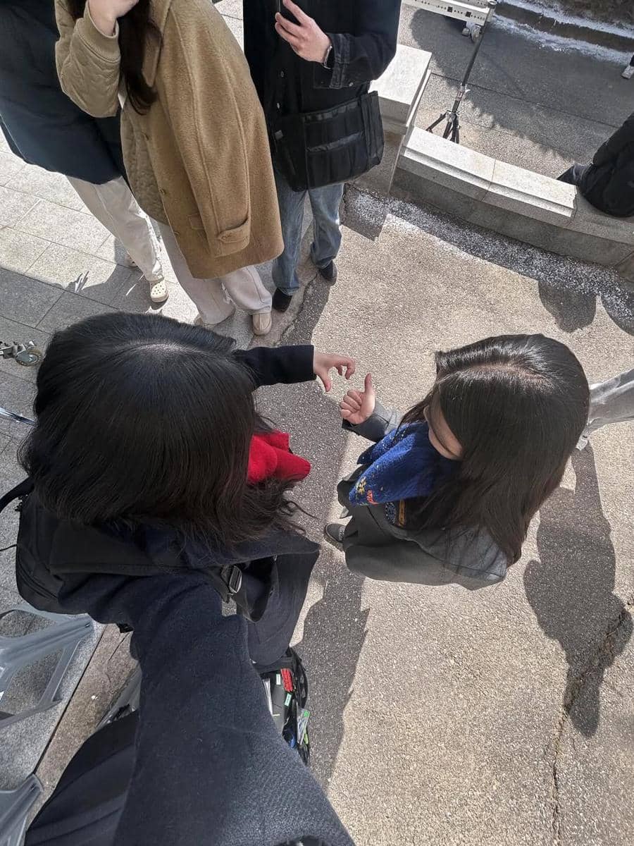 Dua perempuan berambut panjang berbicara dan saling berinteraksi di luar ruangan saat proses syuting drama Korea.