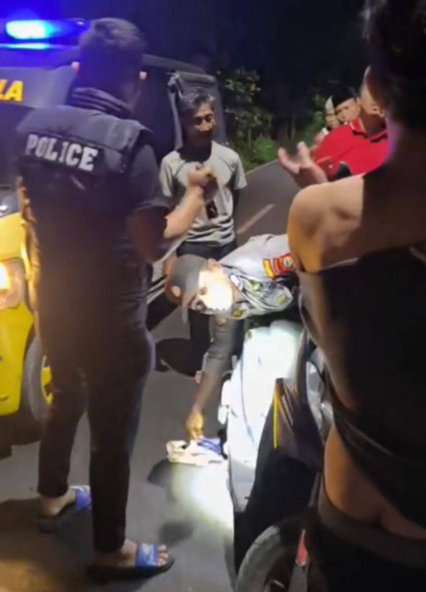 Petugas polisi memeriksa bagasi sepeda motor dan menemukan barang bukti celana dalam curian di lokasi penangkapan malam hari.