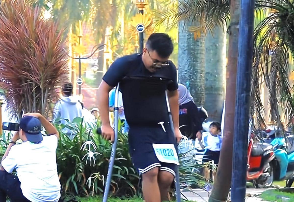 Seorang peserta menggunakan kruk dengan nomor dada 51020 berpartisipasi dalam Malang Half Marathon 2026 di area taman kota.