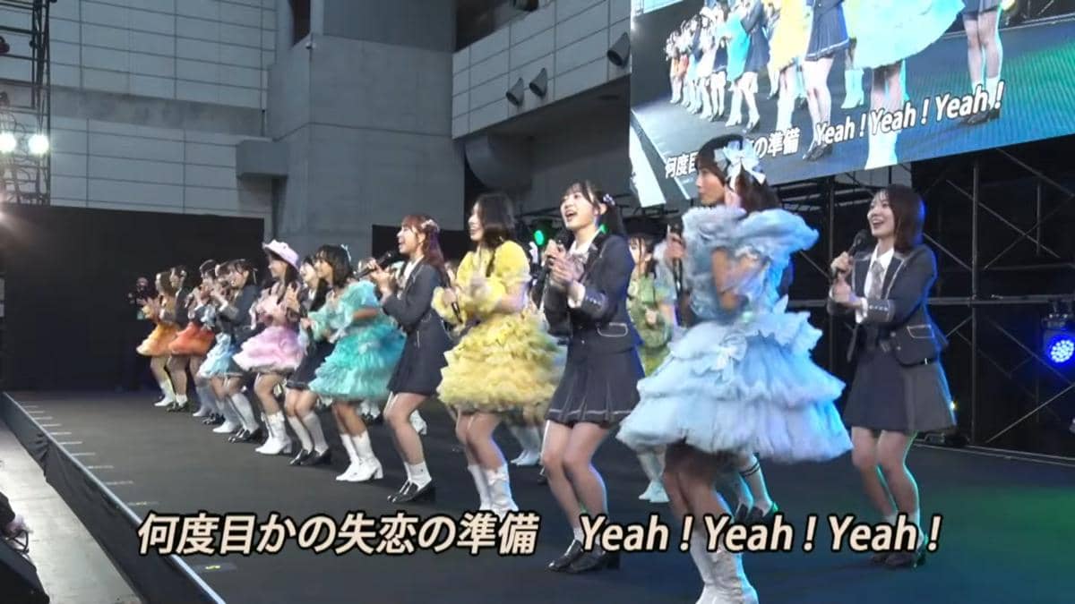 Anggota JKT48 tampil menari dan bernyanyi di atas panggung dalam acara handshake AKB48 2026 dengan kostum berwarna cerah.
