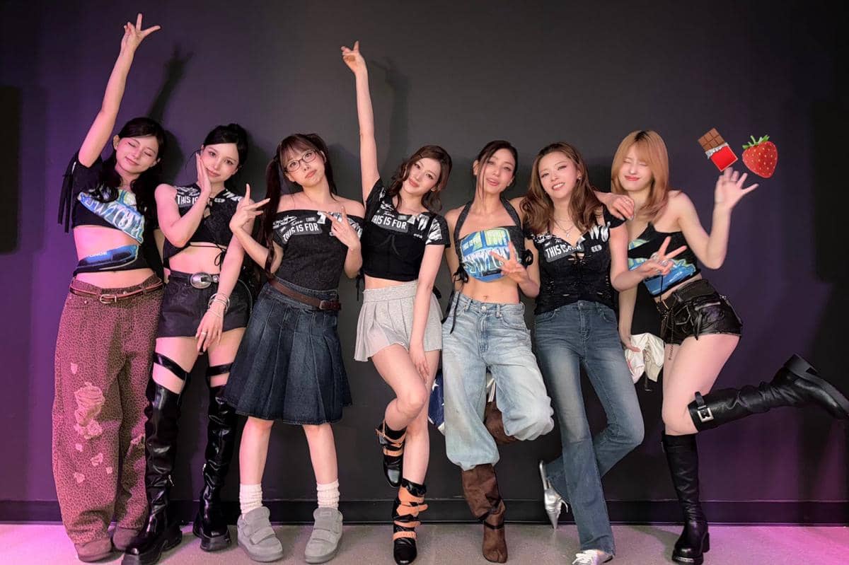 Tujuh anggota grup musik perempuan berpose bersama di depan latar hitam dengan pakaian kasual bergaya modern dan ekspresi ceria.